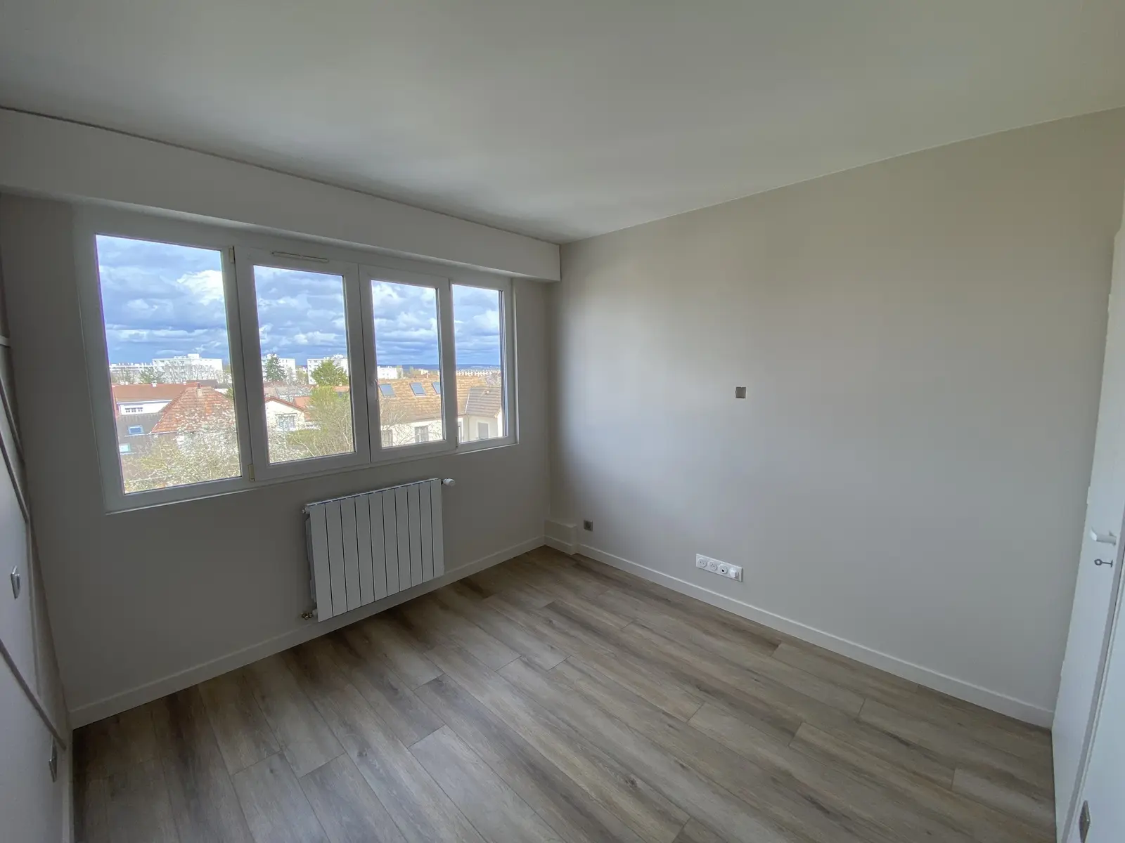 Chambre récemment rénovée. Les murs sont gris clair, et le plafond blanc renforce la luminosité. Le sol est en parquet imitation bois clair, ajoutant une touche chaleureuse.