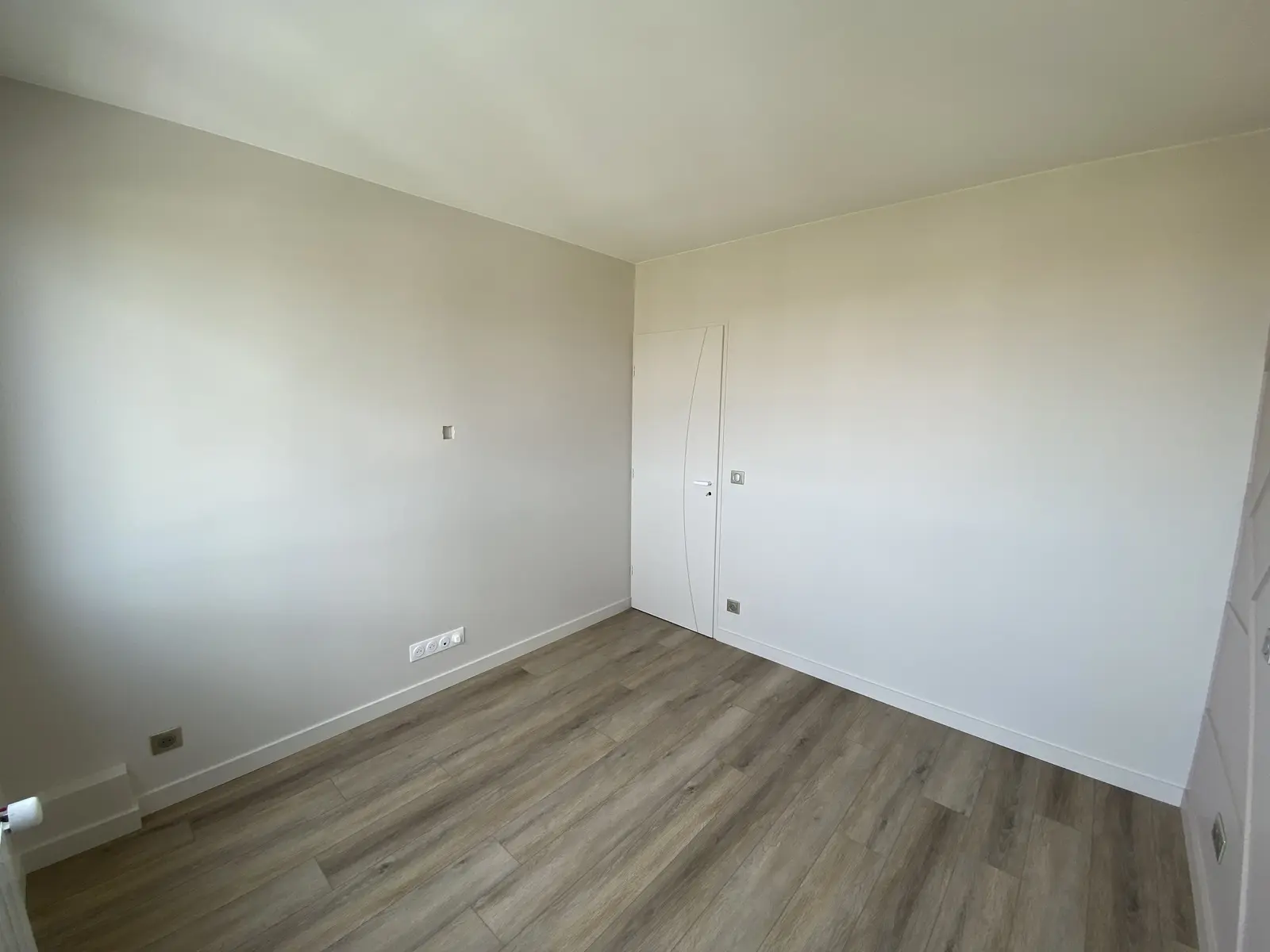 Chambre rénovée aux murs gris clair et parquet immitation bois.