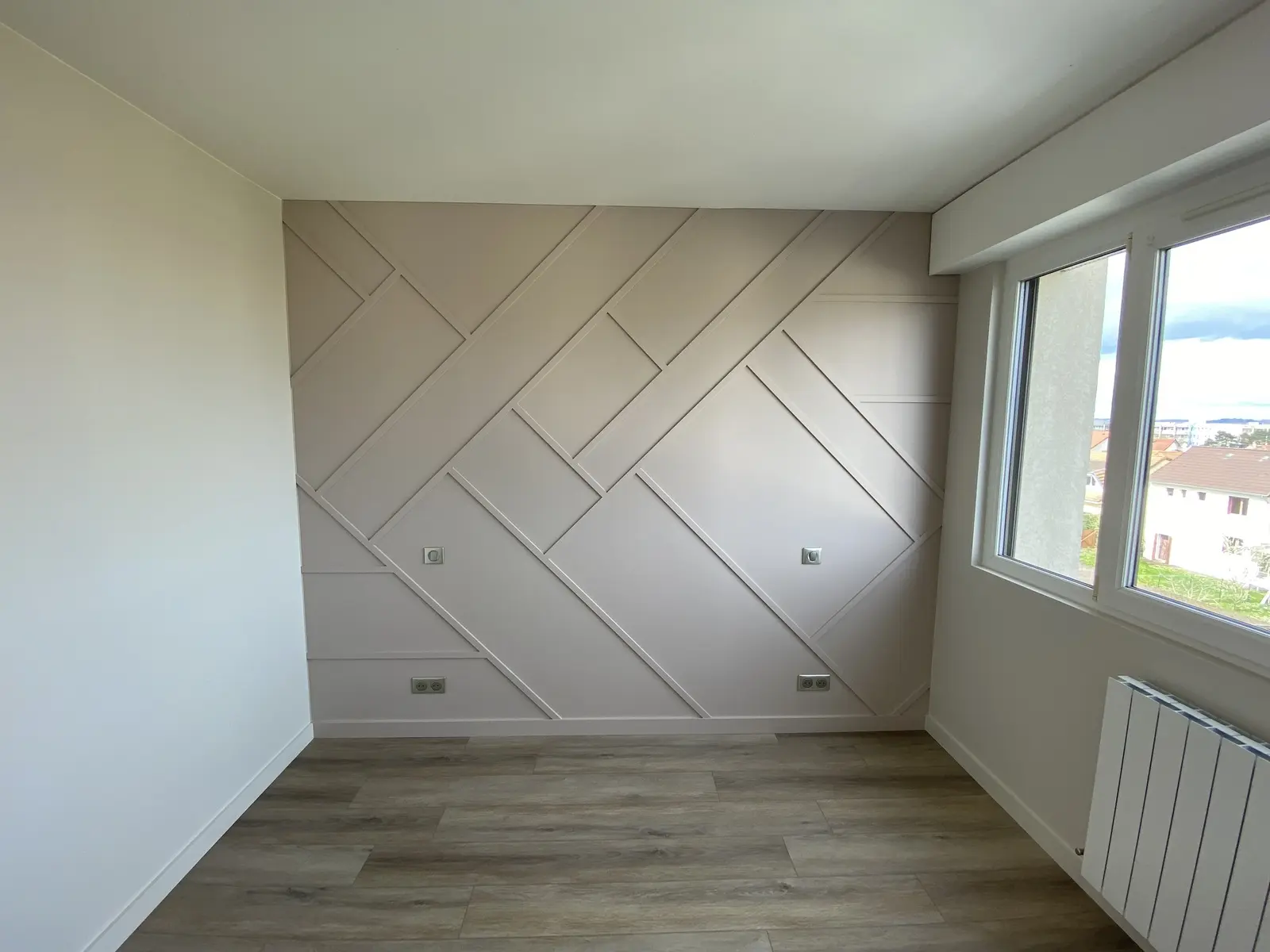 Chambre récemment rénovée. Le mur principal, peint en taupe, est habillé de tasseaux en relief formant un motif géométrique élégant.