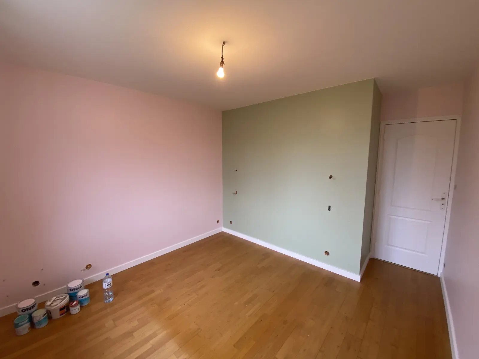 Chambre rénovée avec un mur vert, en contraste avec les autres murs ainsi que les portes et encadrements peints en rose.