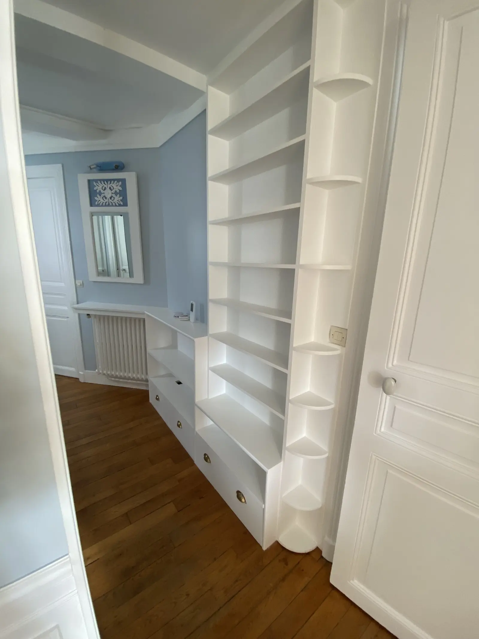 Vue d'un autre angle du couloir aux murs bleu-gris pâle et moulures blanches. Les lignes classiques et les tons doux renforcent l'élégance de l'espace.