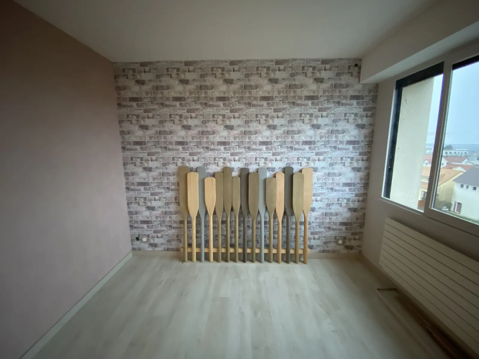 Chambre récemment rénovée avec un mur habillé d'un papier peint imitation brique gris clair, apportant du caractère à l'espace. Les autres murs sont peints en rose pâle, créant une ambiance douce et contemporaine.