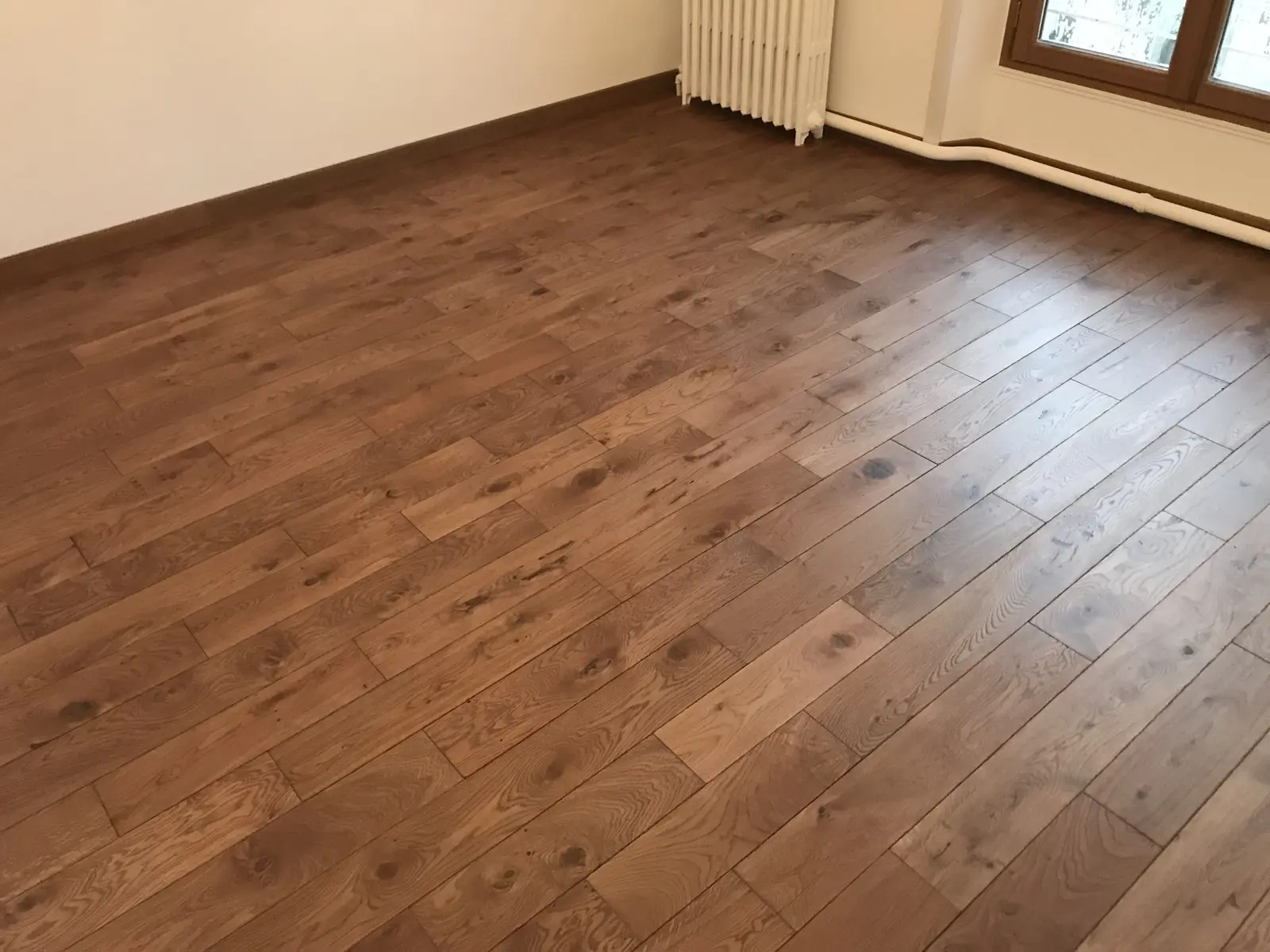 Sol en parquet collé, pose droite. Les lames sont parfaitement alignées, sans espacement visible entre elles. Travail précis et soigné.