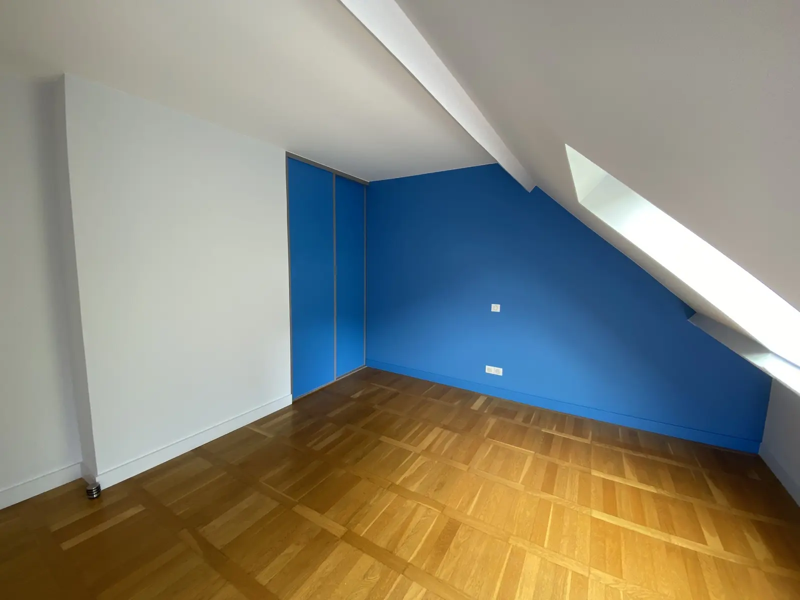 Chambre rénovée où un mur bleu apporte une touche de couleur, tandis que les autres murs, portes et encadrements restent blancs.