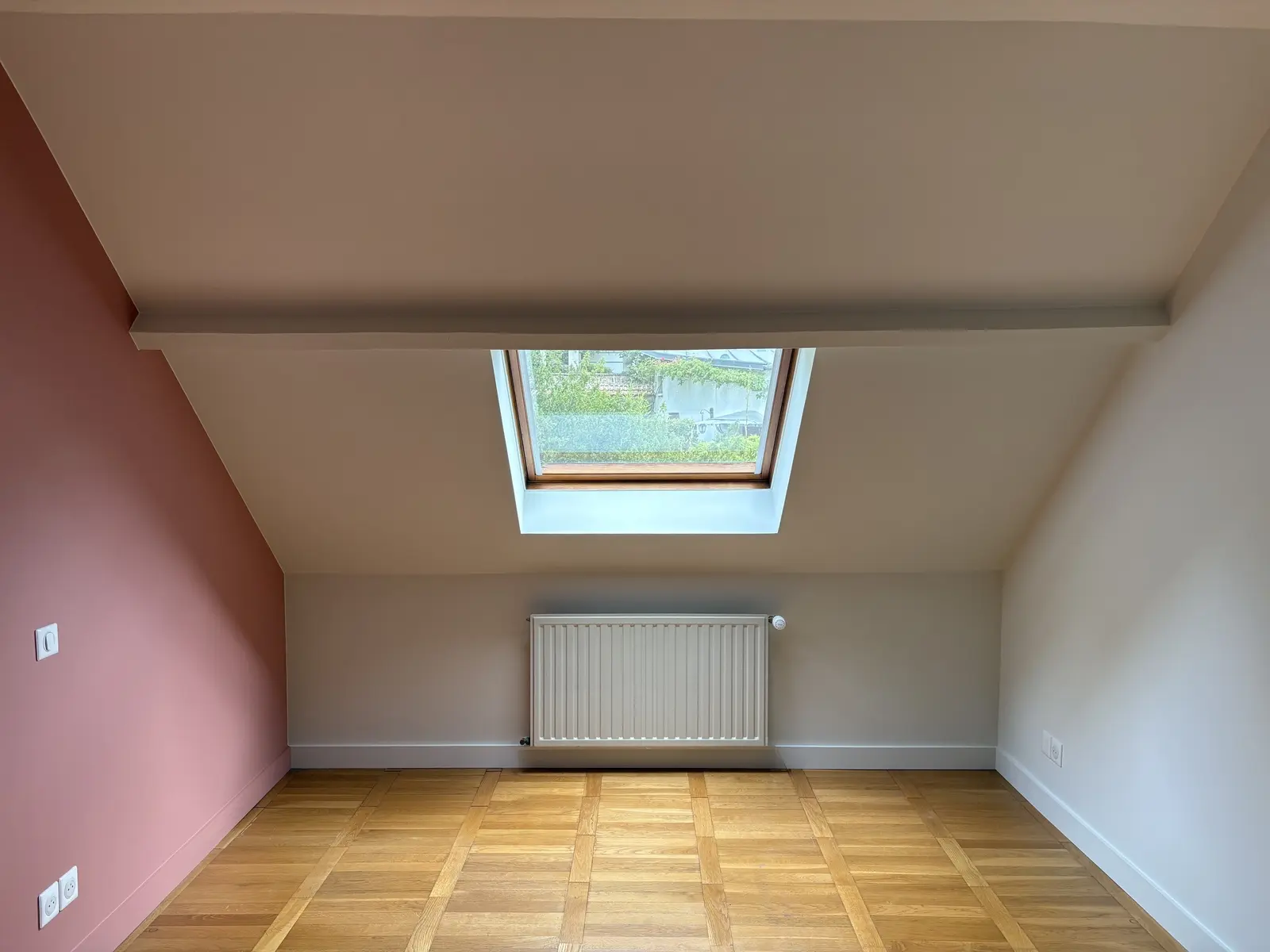 Chambre rénovée où un mur rose apporte une touche de couleur, tandis que les autres murs, portes et encadrements restent blancs.