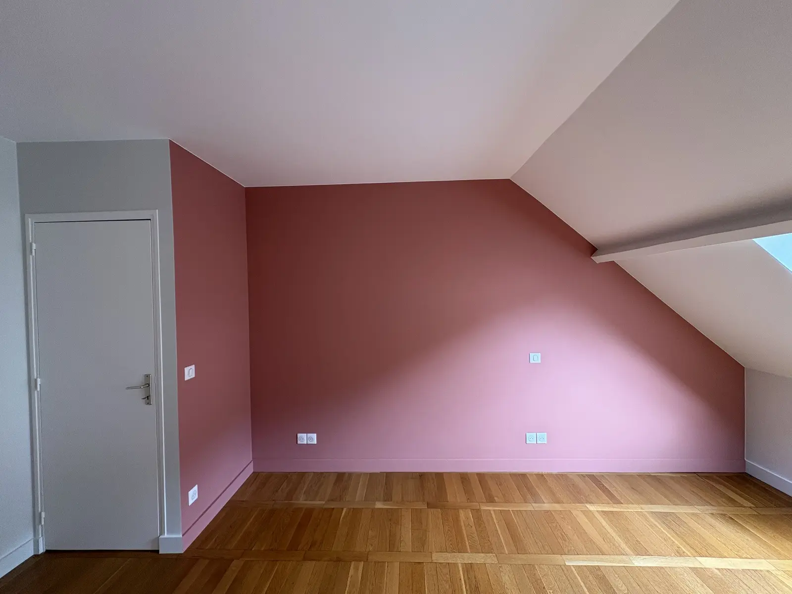 Chambre rénovée avec un mur rose, en contraste avec les autres murs ainsi que les portes et encadrements peints en blanc.
