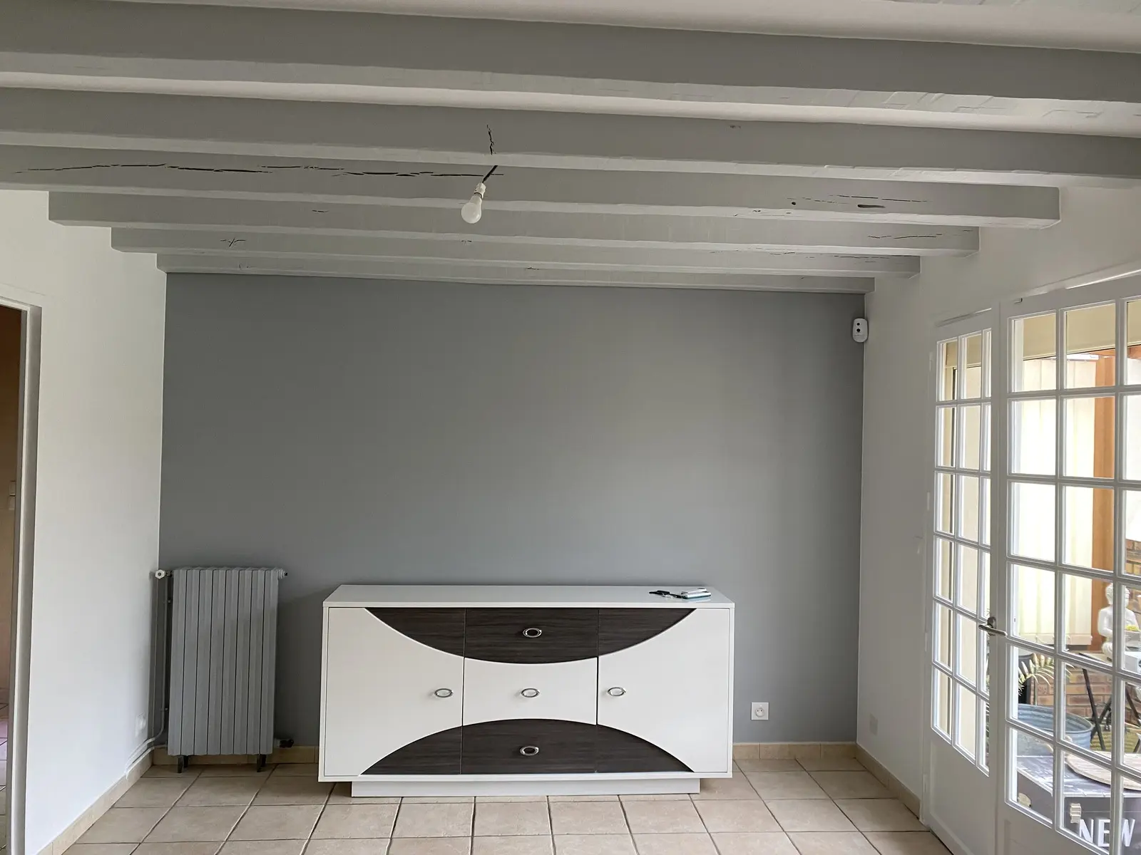 Salon rénové avec poutres apparentes peintes en gris clair, finition lisse et soignée.