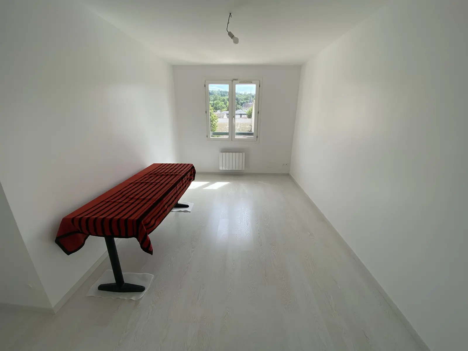 Pièce rectangulaire fraîchement repeinte en blanc, avec un sol clair effet bois.