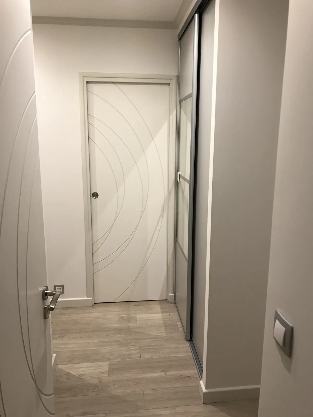 montre un couloir avec plusieurs portes. La particularité réside dans la peinture des portes blanches, où les rainures sont accentuées par une couleur plus foncée, créant un effet de design et de contraste. Cela met en valeur les motifs et la texture des portes.
