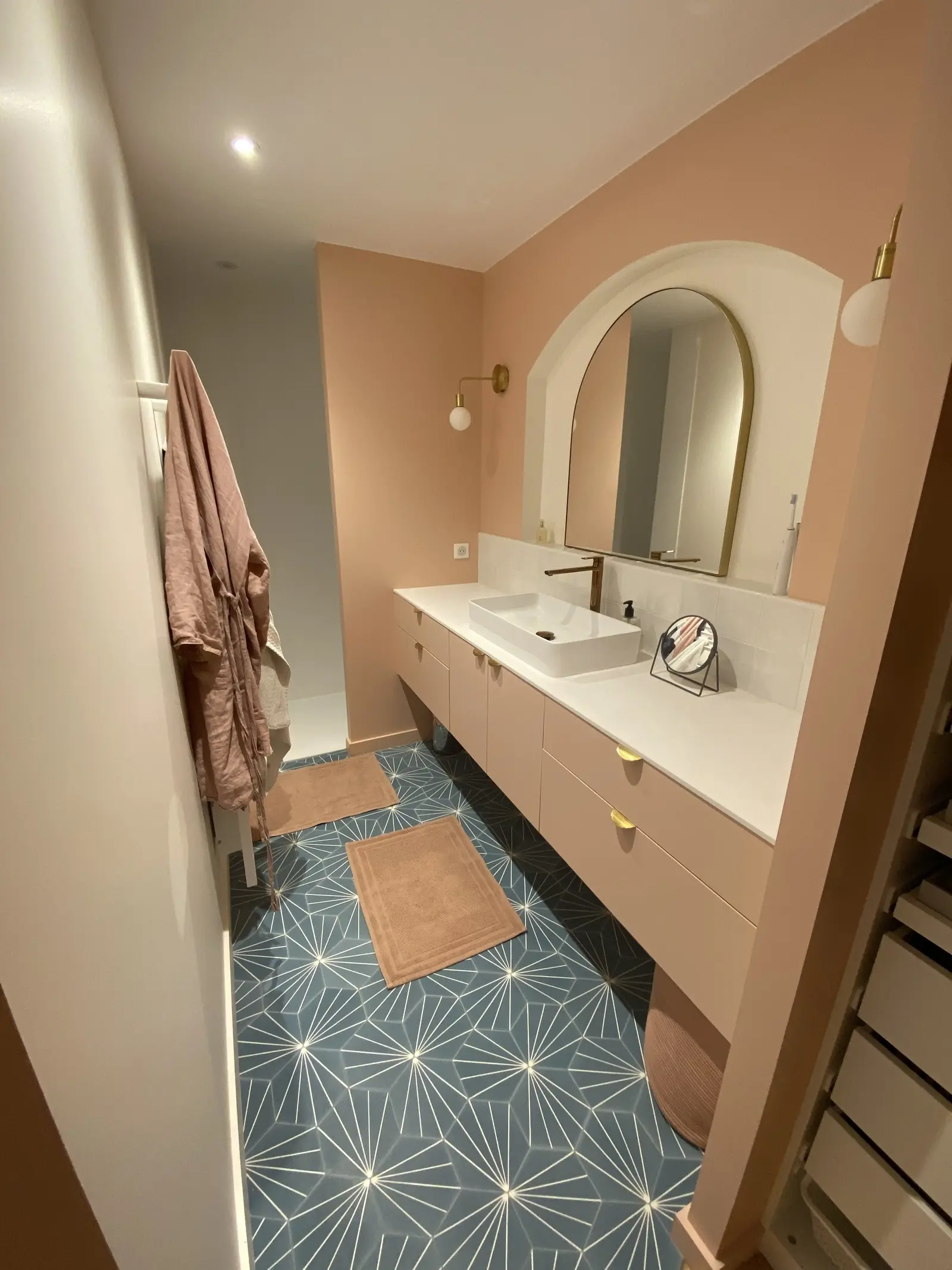 Salle de bain contemporaine avec un meuble vasque peint dans le même ton rose poudré que les murs. Une arche peinte en blanc encadre élégamment le miroir, créant un contraste subtil et raffiné.
