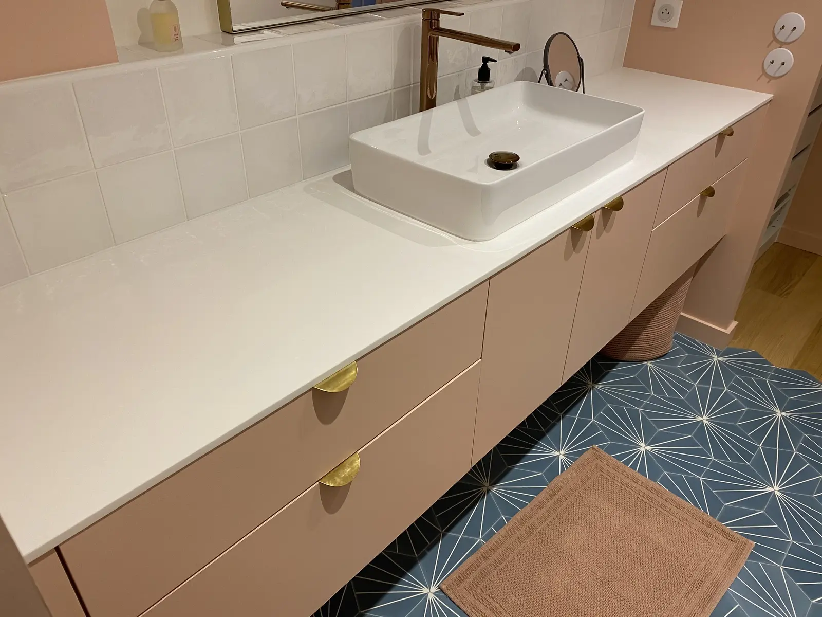 Salle de bain avec meuble vasque rose poudré et mur habillé de carreaux blancs.