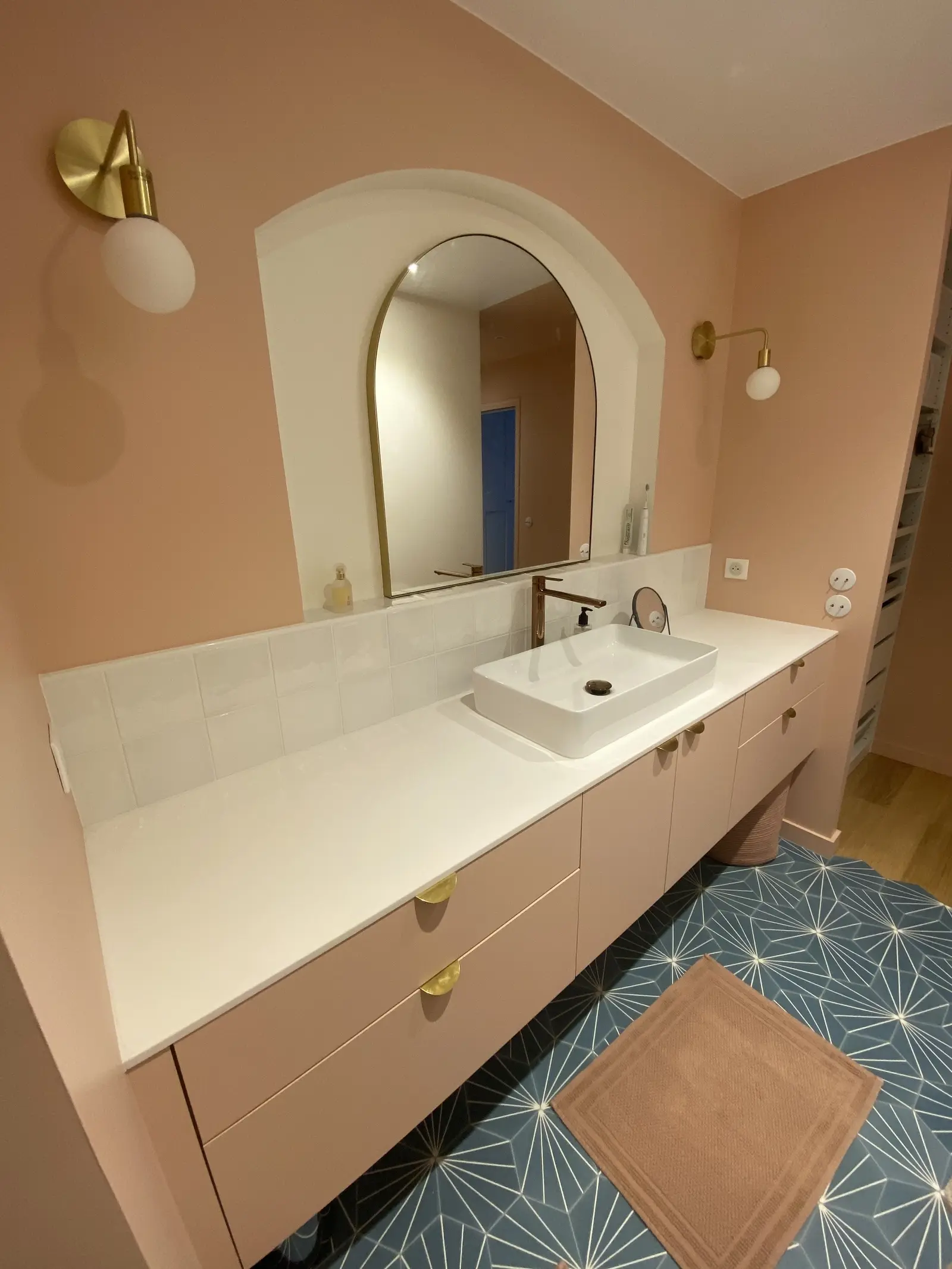 Autre vue d'une salle de bain contemporaine où le meuble vasque se fond dans les murs rose poudré. L'arche blanche autour du miroir apporte contraste et élégance.