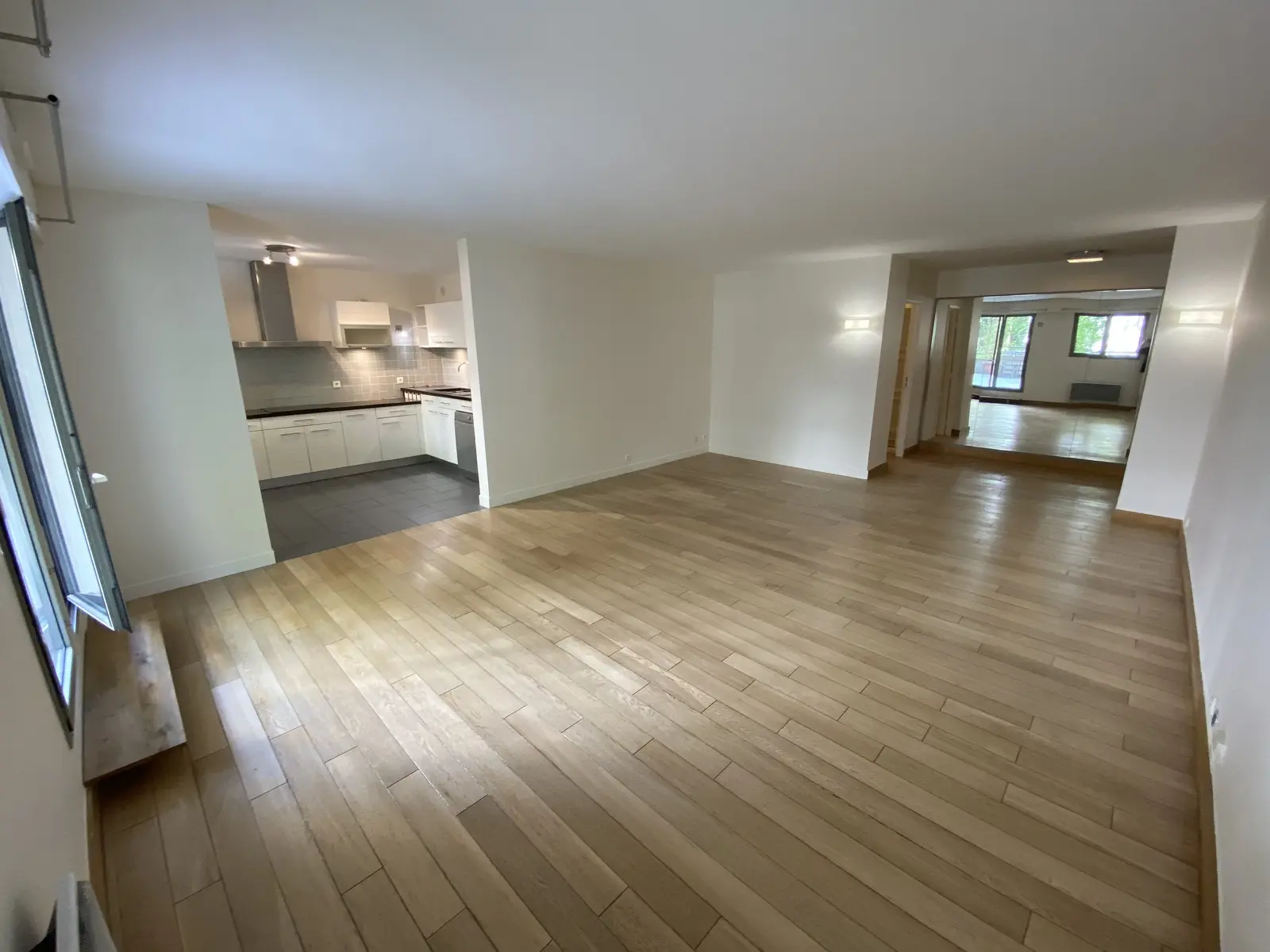 Vaste espace de vie avec un parquet clair en bois, récemment poncé et parfaitement lisse. La lumière met en valeur la qualité du bois et la finesse du travail de ponçage.