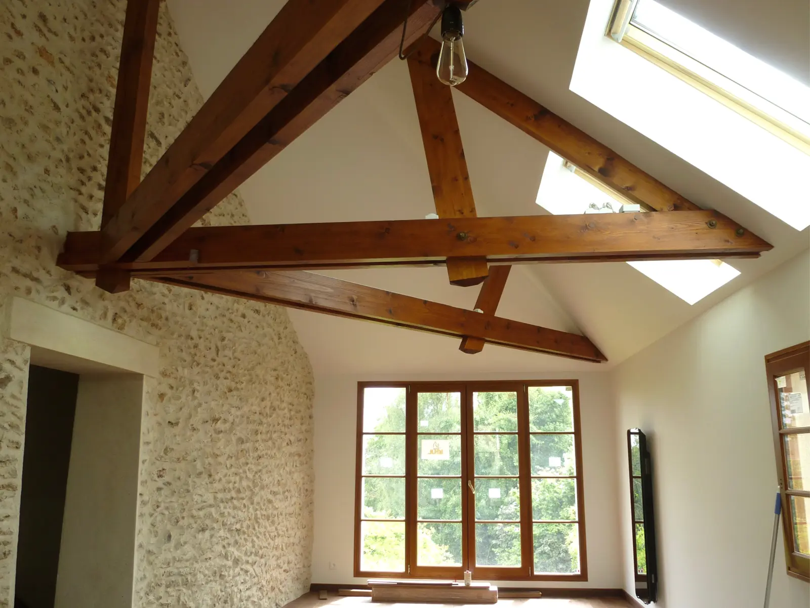 Poutres en bois apparentes, de couleur brun-roux, qui forment une charpente imposante et élégante.  La rénovation met en avant la beauté du bois et du matériau d'origine, créant un espace harmonieux entre tradition et modernité.